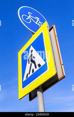 Segnaletica stradale per la pista ciclabile e segnaletica di attraversamento pedonale sullo sfondo blu del cielo Foto Stock