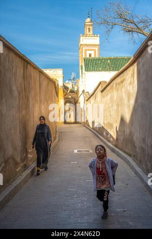 Una ragazza e sua madre passeggiano per un vicolo illuminato dal sole nella medina di Fez. Foto Stock