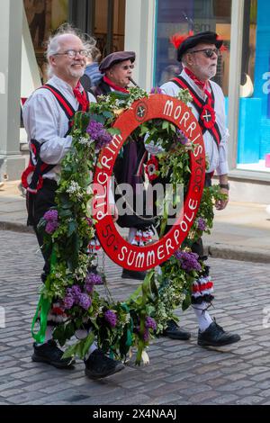 4 maggio 2024. Il Guildford Summerpole Festival si è svolto oggi nel centro della città, un'usanza tradizionale del folclore inglese per celebrare il giorno di maggio e dare il benvenuto all'estate. L'evento annuale gestito dai ballerini Guildford Pilgrim Morris prevede una processione fino alla High Street, esibizioni di morris danzanti da parte degli uomini Pilgrim Morris e diversi gruppi di ballo ospiti, seguite dall'erigere il palo estivo (invece di un tradizionale maypole) nei terreni del castello di Guildford, e ulteriori danze. Nella foto: Due ballerini Pilgrim Morris portano la ghirlanda lungo la strada principale durante la processione. Foto Stock