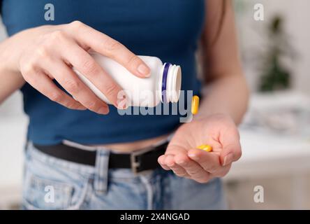 Una giovane donna tiene in mano pillole gialle, una femmina prende integratori e vitamine da una bottiglia, primo piano Foto Stock