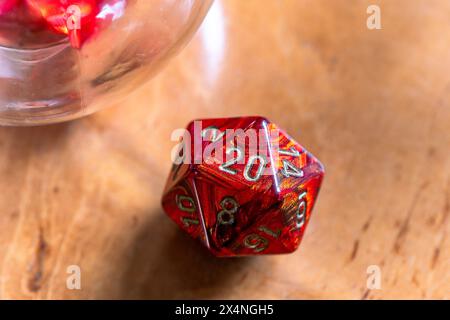 Primo piano di un vivace dado rosso D20, che enfatizza i dettagli su un caldo sfondo in legno, perfetto per giochi e temi fantasy. Foto Stock