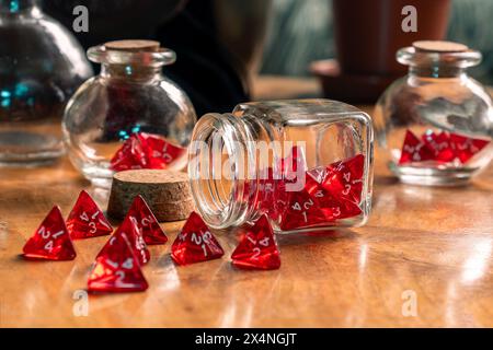 Dadi rossi versati da un vaso di vetro su un tavolo in legno rustico, catturando un momento di gioco in un'elegante disordinatezza Foto Stock