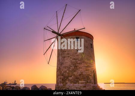 Storico mulino a vento contro un cielo all'alba di colore viola-arancione vicino al mare, crepuscolo, Mandraki OAT, Rodi, Dodecaneso, isole greche, Grecia Foto Stock