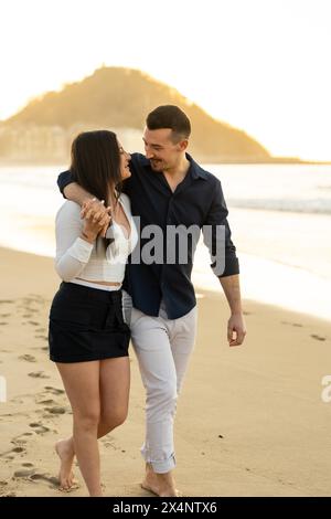 Foto verticale di una coppia giovane ed elegante che si gode una passeggiata al tramonto lungo una spiaggia Foto Stock