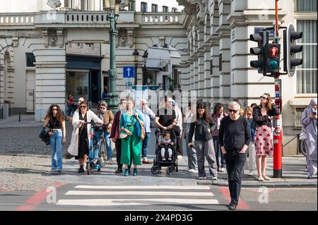 Bruxelles regione capitale, Belgio - 1° maggio 2024 - folla di pedoni in attesa all'incrocio mentre un uomo ignora il semaforo rosso Foto Stock