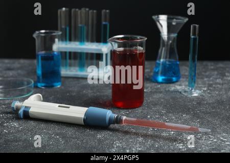 Analisi di laboratorio. Micropipetta e vetreria diversa su tavolo grigio Foto Stock