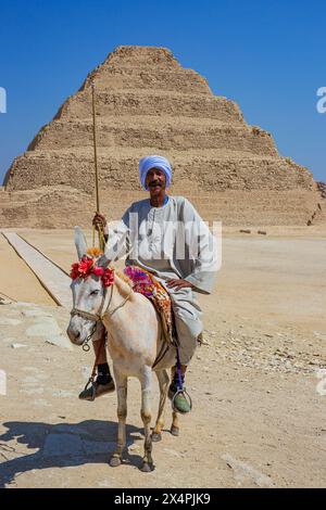 Un uomo egiziano in abito tradizionale su un asino presso la piramide a gradoni di Zoser (terza dinastia) a Saqqara, in Egitto Foto Stock