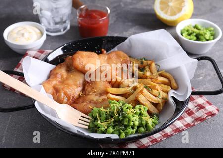 Gustoso pesce, patatine, salse e piselli sul tavolo grigio, primo piano Foto Stock