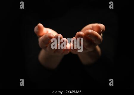 Religione. Donna con le palme aperte che prega su sfondo nero, primo piano Foto Stock