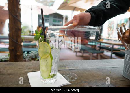 Limonata con limone fresco su sfondo tavolo di legno. la mano di un uomo in una manica nera versa una bevanda gassata in un alto vetro trasparente, in cui Foto Stock
