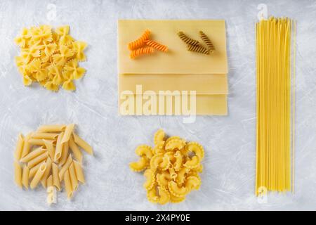 Set di pasta italiana cruda su sfondo in cemento grigio, vista dall'alto Foto Stock