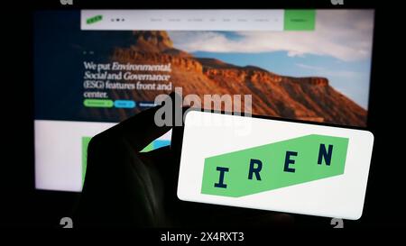 Persona che possiede uno smartphone con il logo della società mineraria australiana Iris Energy Ltd. (IREN) davanti al sito web. Mettere a fuoco il display del telefono. Foto Stock