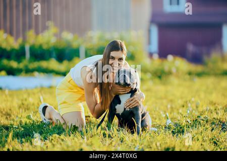 Il proprietario gira la testa del cane verso la macchina fotografica per scattare foto insieme, seduto sul prato vicino alla casa di campagna la sera d'estate, la giovane donna caucasica scatta foto con una A. Foto Stock