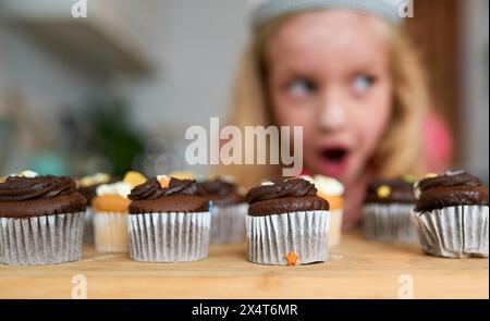 Sorpresa, cupcake e bambino a tavola in casa e affamati di cioccolato o torta alla festa di compleanno. Eccitato, ragazza e festa all'evento con cibo Foto Stock