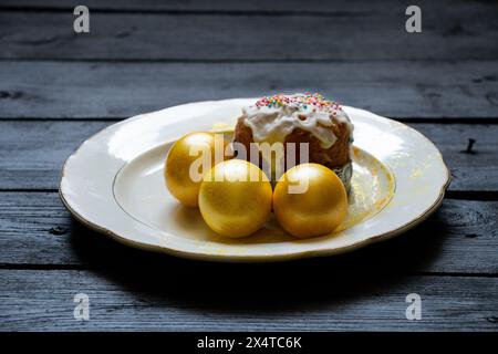 La torta di Pasqua fatta in casa e le uova dorate si stagliano su un piatto su una tavola nera, festa di Pasqua in Ucraina Foto Stock