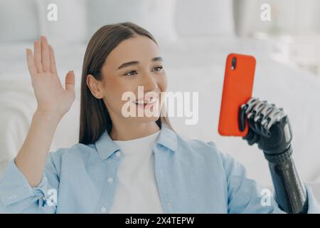 Giovane donna allegra con braccio protesico che crea un vlog, che abbraccia con facilità tecnologie avanzate. Foto Stock