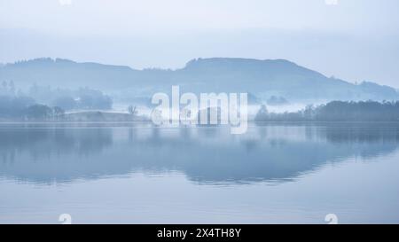 Splendida immagine di paesaggio tranquillo della mattina nebbiosa di primavera su Windermere nel Lake District con barche ormeggiate sul lago e lontane cime nebbiose Foto Stock