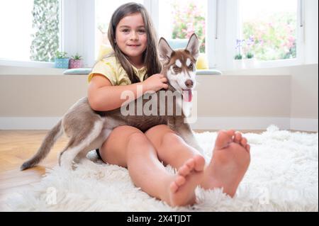 Sorridente ragazza e il suo cucciolo Siberian Husky sul tappeto a casa. Foto di alta qualità Foto Stock