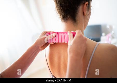 Osteopata del raccolto applicando del nastro per kinesiologia sul collo della paziente in clinica Foto Stock