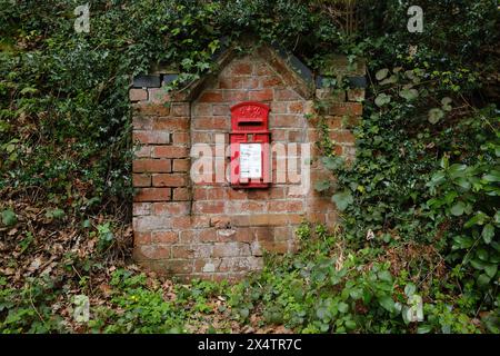 Casella di lettere rossa in un muro di mattoni vicino a una corsia di campagna in Inghilterra Foto Stock