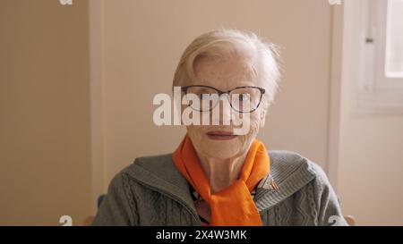 Donna anziana che guarda la macchina fotografica seduta in una casa di riposo Foto Stock