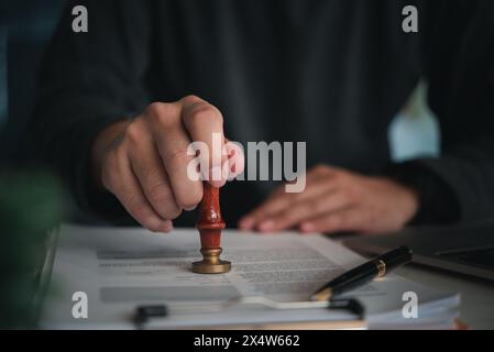 Persona concentrata che posiziona un sigillo su un documento ufficiale con francobollo di cera rosso in un ambiente professionale Foto Stock
