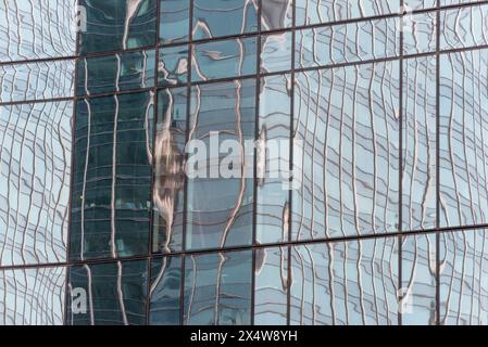 Il riflesso di un edificio nella finestra di vetro di un edificio. Il riflesso è distorto e ondulato, dando l'impressione di una superficie d'acqua Foto Stock