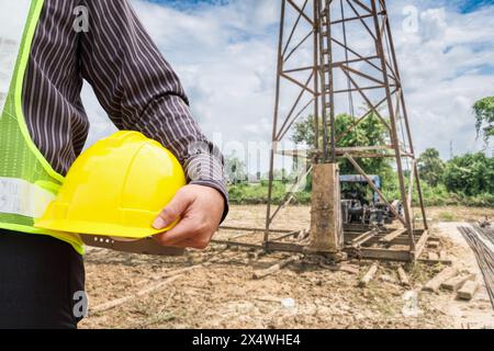 Uomo d'affari asiatico ingegnere lavoratore in casco protettivo e Blueprints carta a portata di mano a casa cantiere Foto Stock