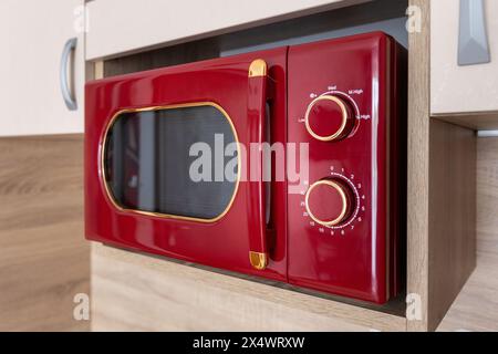 Moderno forno a microonde rosso per cucinare gli alimenti sullo scaffale della cucina e sull'armadietto Foto Stock
