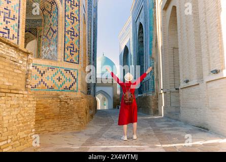 Donna turistica in abiti rossi si trova nello Shah-i-Zinda Ensemble a Samarcanda, Uzbekistan Foto Stock