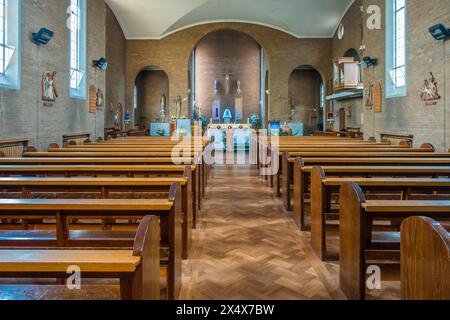 Una vista lungo la navata di una chiesa con tradizionali pali di legno per sedersi Foto Stock