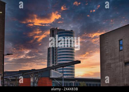 Un tramonto spettacolare su un paesaggio urbano moderno con un alto edificio in vetro e strutture circostanti. Foto Stock