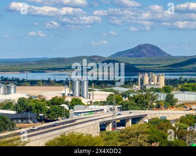 Vista aerea di Gaborone drone prospettiva del ponte di cavalcavia dell'area industriale con traffico, con diga di Gaborone sullo sfondo e colline e montagne suonate Foto Stock