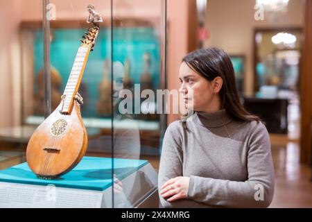 Visitatore del museo femminile che esamina gli antichi strumenti musicali Foto Stock