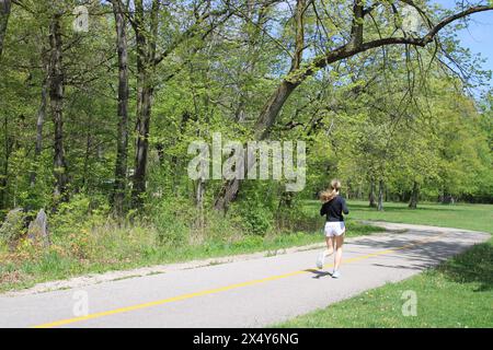 Giovane donna con una coda di pony bionda che corre sul North Branch Trail e si dirige verso una curva a Harms Woods a Skokie, Illinois Foto Stock