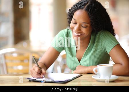 Felice donna nera che compila il modulo in una terrazza del ristorante Foto Stock