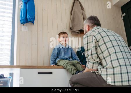 Padre che aiuta figlio a prepararsi per l'asilo, asilo. Mettere le scarpe. Foto Stock