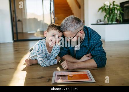 Padre che mostra al figlio un sistema di casa intelligente, che regola le funzioni domestiche, l'illuminazione, le telecamere di sicurezza, le serrature delle portiere e le impostazioni del termostato o del riscaldamento intelligenti Foto Stock