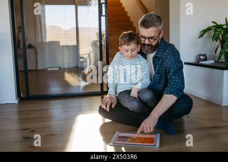 Padre che mostra al figlio un sistema di casa intelligente, che regola le funzioni domestiche, l'illuminazione, le telecamere di sicurezza, le serrature delle portiere e le impostazioni del termostato o del riscaldamento intelligenti Foto Stock