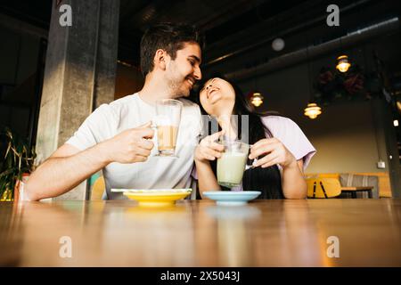 Giovane coppia sorridente seduta in un bar. Coppia in un appuntamento in un bar locale che beve caffè e tè matcha. Foto Stock