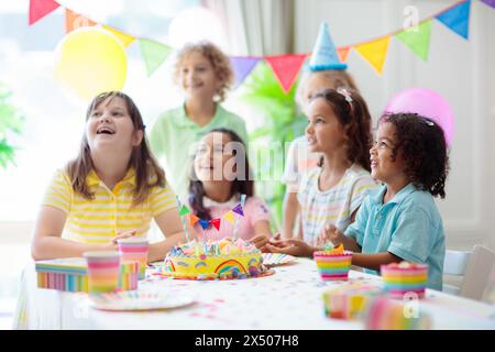 Festa di compleanno dei bambini. I bambini festeggiano con torte colorate e regali. Piccolo ragazzo curly soffiando candele e l'apertura di regali di compleanno. Foto Stock