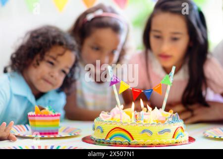 Festa di compleanno dei bambini. I bambini festeggiano con torte colorate e regali. Piccolo ragazzo curly soffiando candele e l'apertura di regali di compleanno. Foto Stock