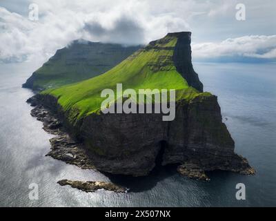Panoramica aerea di un piccolo faro bianco situato sul bordo di una rupe enorme e l'isola di Kalsoy. Kalsoy è isolata una piccola isola nel n. Foto Stock