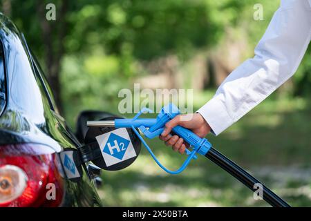 L'uomo ha un ugello di alimentazione dell'idrogeno. Rifornimento di carburante per auto con idrogeno. Concetto Foto Stock