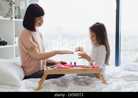 Una bambina carina impara a dipingere le unghie applicando il lucido sulle mani della madre. Foto Stock