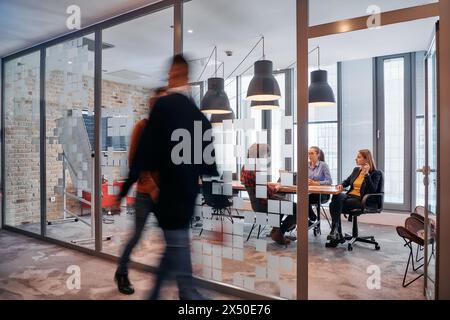 Nel caos dinamico di un ambiente di lavoro, un gruppo di giovani professionisti percorre il corridoio accanto al loro ufficio Foto Stock