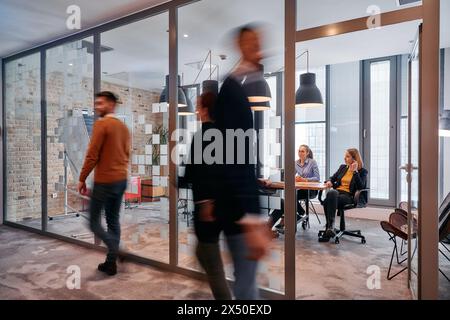 Nel caos dinamico di un ambiente di lavoro, un gruppo di giovani professionisti percorre il corridoio accanto al loro ufficio Foto Stock