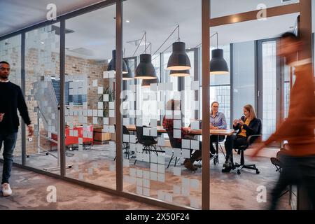 Nel caos dinamico di un ambiente di lavoro, un gruppo di giovani professionisti percorre il corridoio accanto al loro ufficio Foto Stock