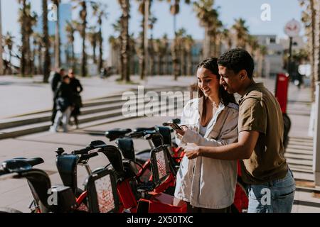 Coppia giovane che si gode una giornata di vento scegliendo le biciclette da una stazione di noleggio a Barcellona. Foto Stock