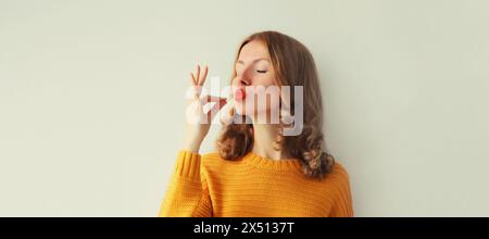 Ritratto di una giovane donna felice che gode di un sapore perfetto, mostra un gesto di delizioso gusto di cibo sullo sfondo dello studio Foto Stock